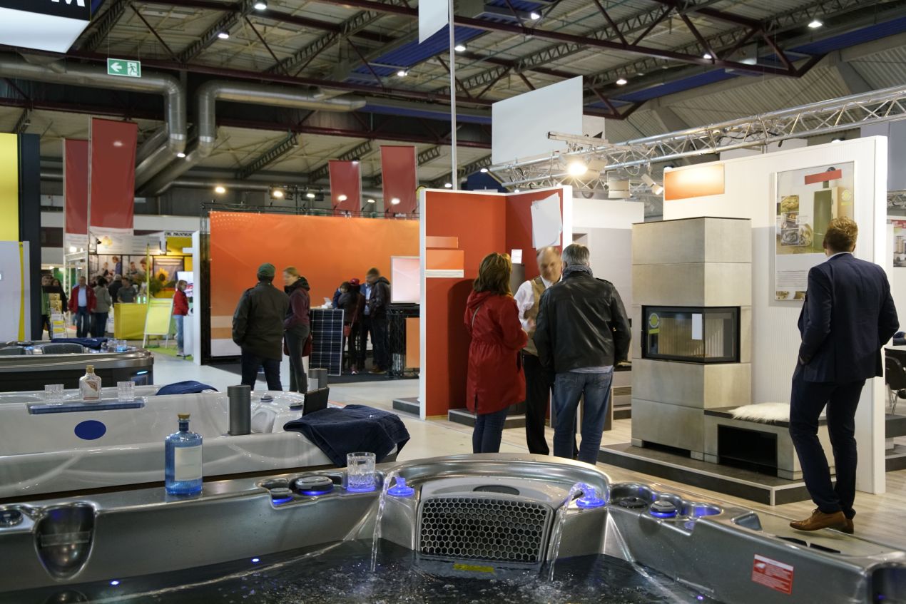 Messestand Set mit Whirlpool und Kamin auf einer Fachmesse, umgeben von Besuchern und Ausstellern in einer modernen Messehalle