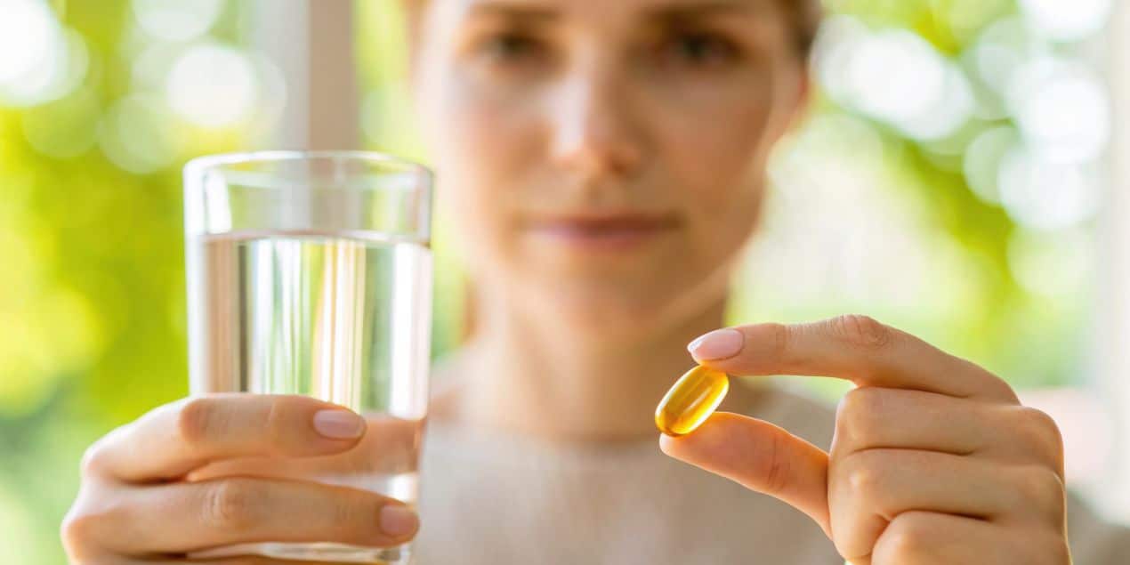 Frau haelt Omega-3 Algenoel-Kapsel und Wasserglas zur taeglichen Einnahme pflanzlicher Vitalstoffe